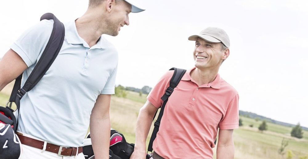 Happy male golfers conversing against clear sky
